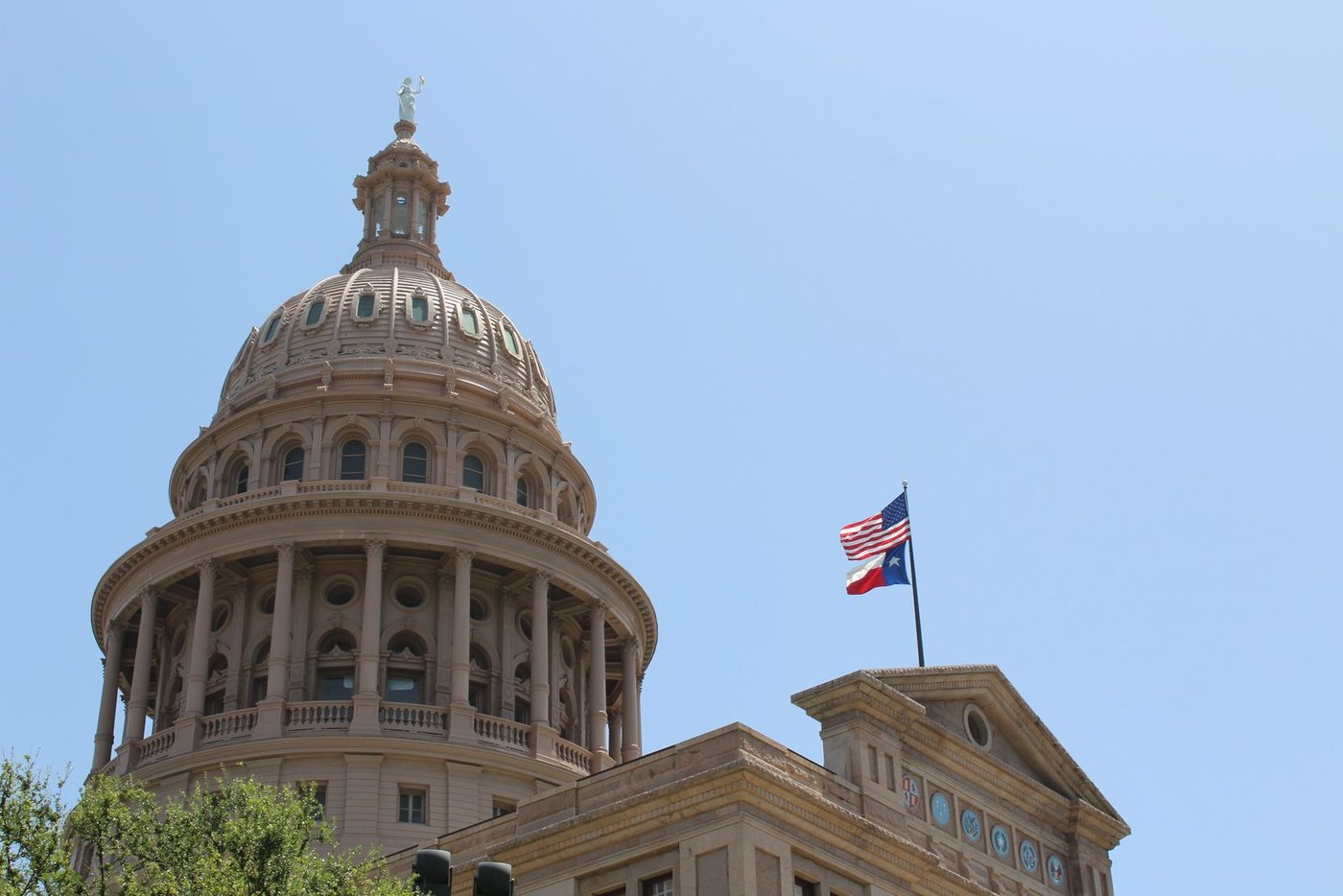 The pink granite dome of the Texas State Capitol in Austin with the Goddess of Liberty statue on top and the US and Texas flags flying