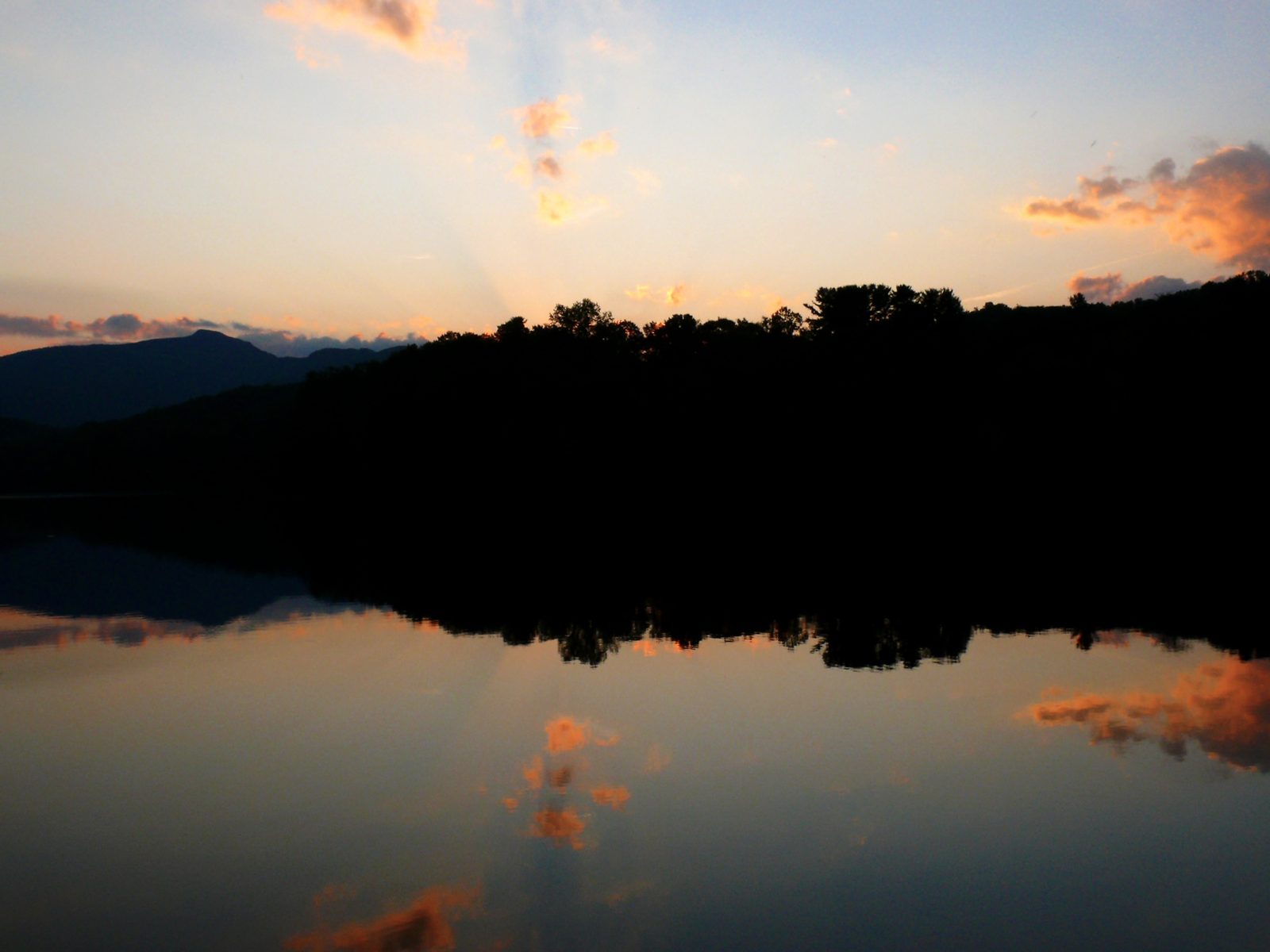 Sunset reflected in the still water of Price Lake on the Blue Ridge Parkway, with dark tree-covered ridges