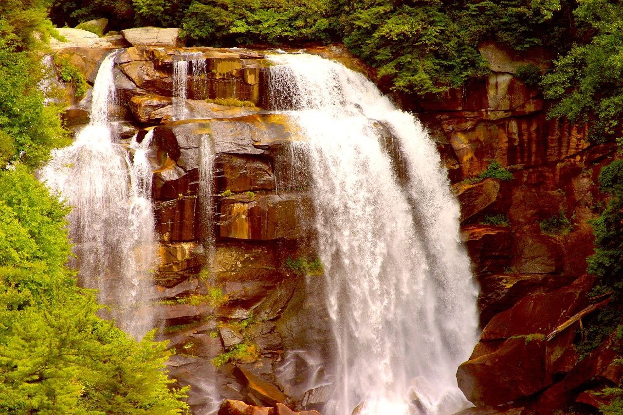 Whitewater Falls pouring in two wide white streams over a tall rock face, framed by green trees