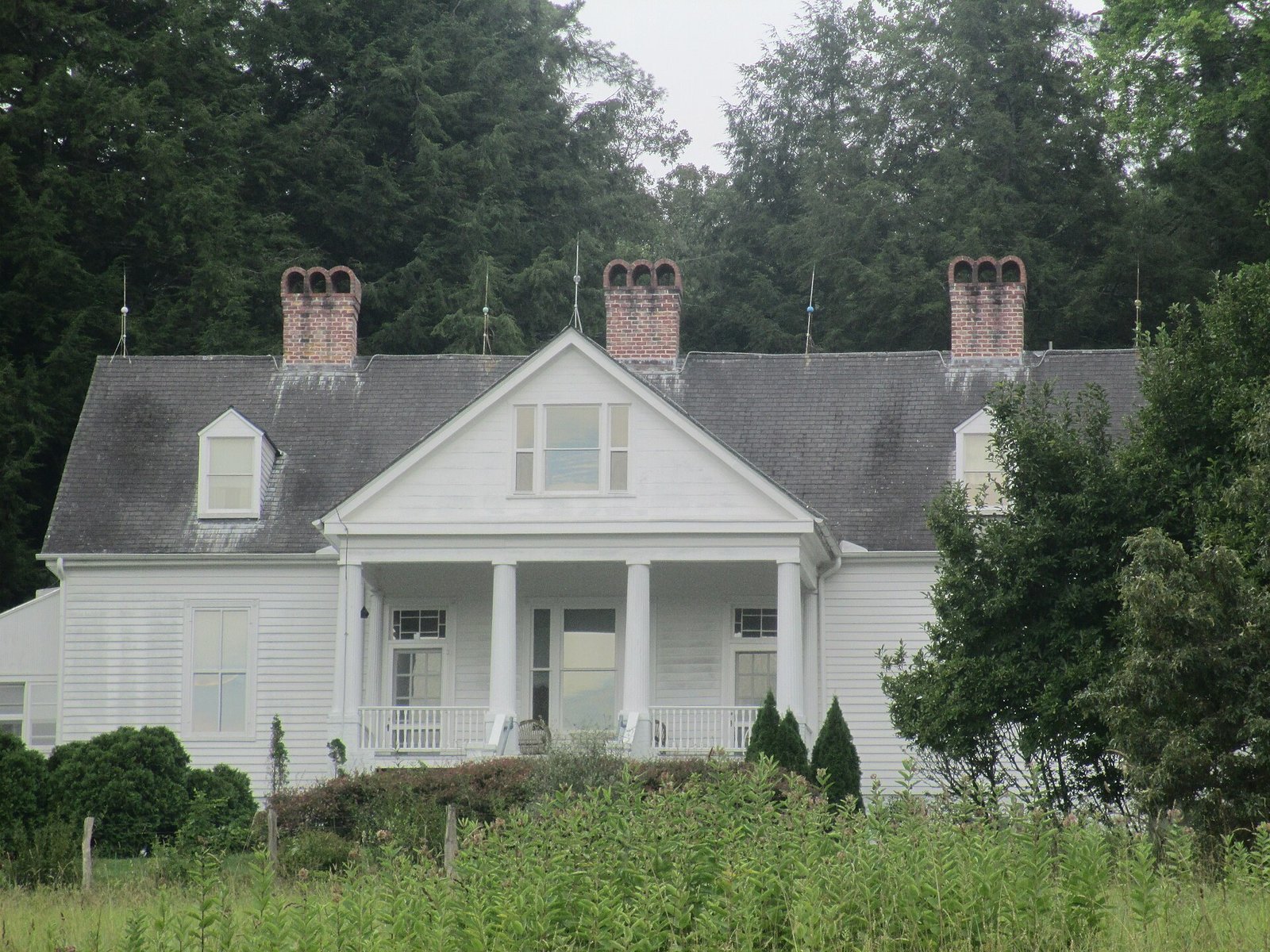 The white two-story Carl Sandburg house with a columned porch and three brick chimneys, surrounded by tall trees