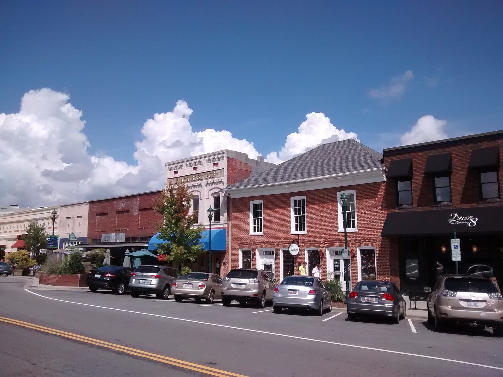 Brick storefronts and parked cars along Main Street in downtown Hendersonville, North Carolina, under a blue sky