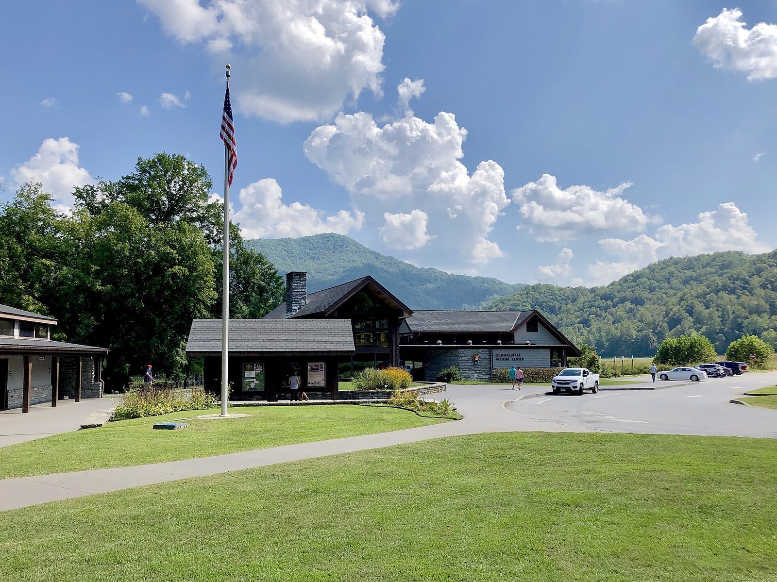 The Oconaluftee Visitor Center with a flagpole in front and green mountains behind it under a blue sky
